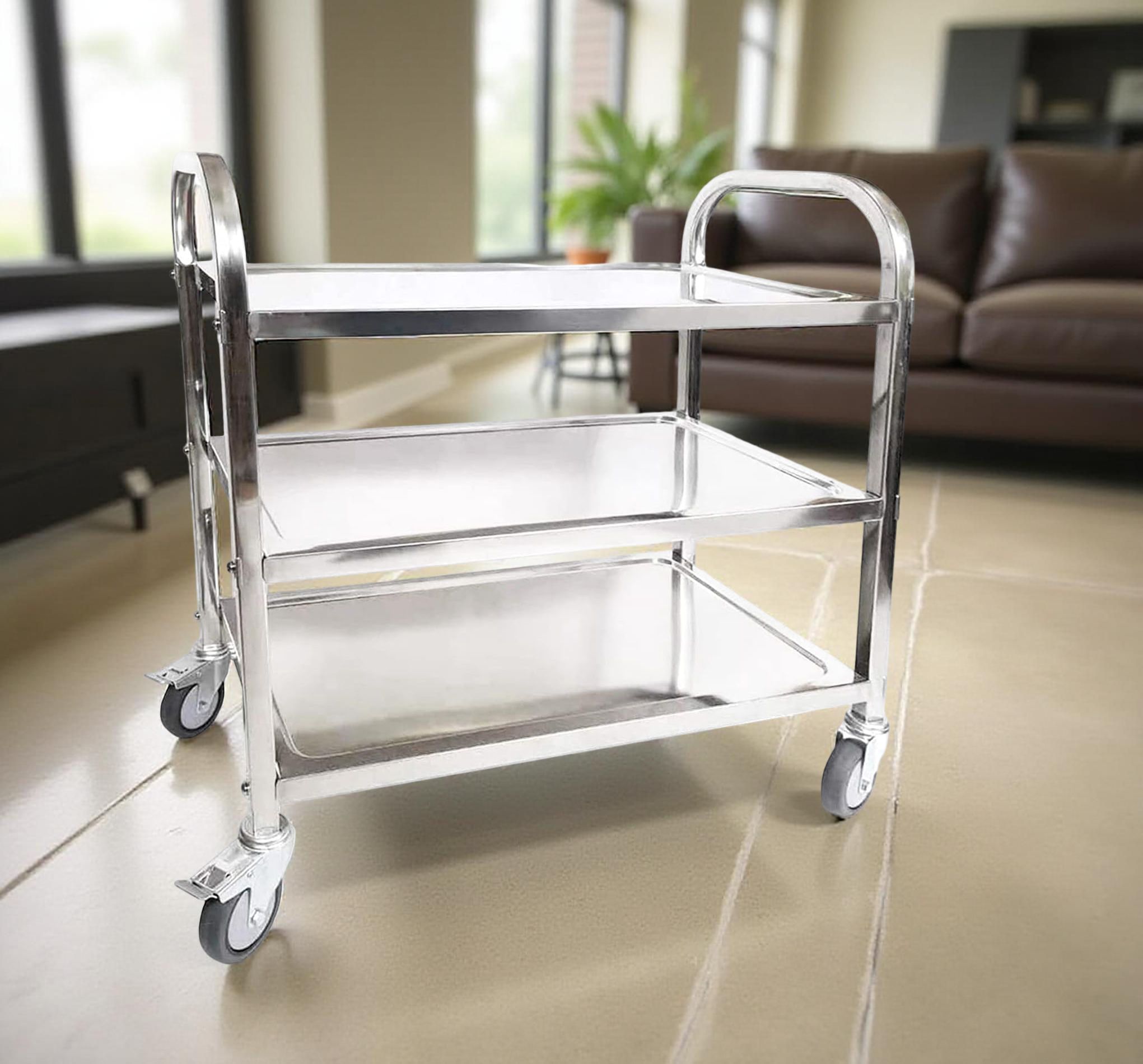 A stainless steel trolley with three tiers, designed for medical use, positioned in a well-lit room with a couch in the background.
