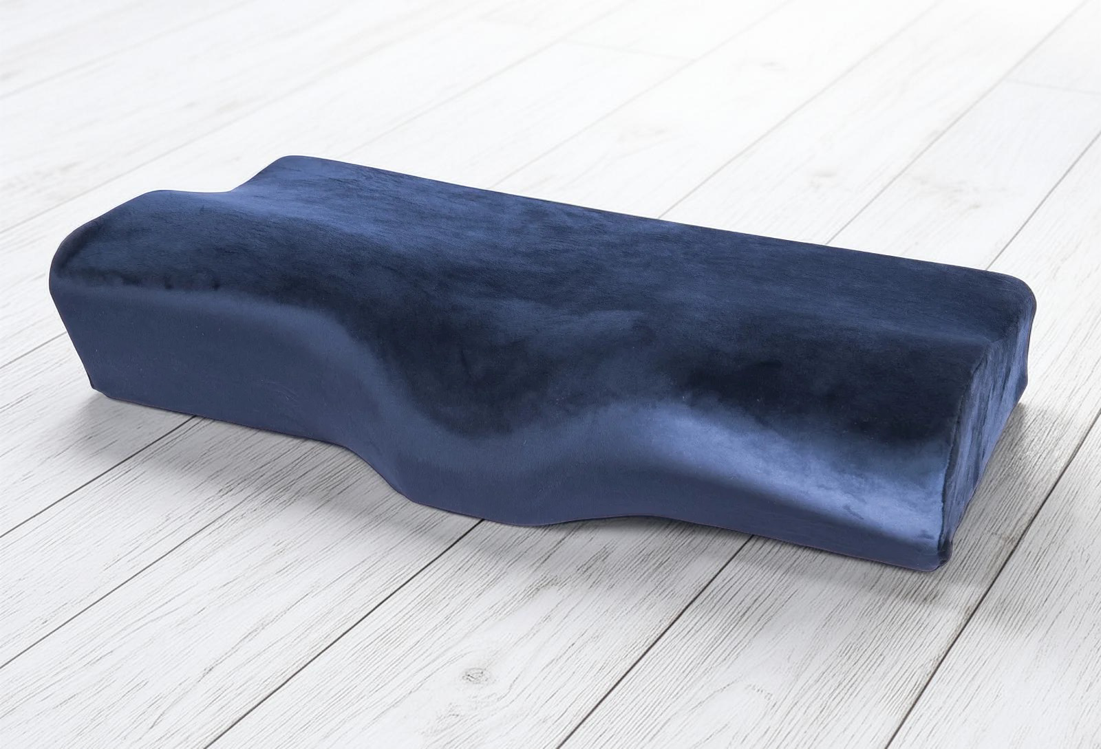 A navy blue memory foam pillow with a contoured design, placed on a wooden floor.